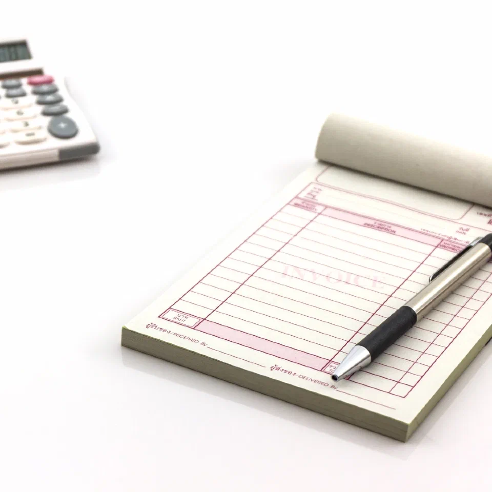 A carbonless invoice pad with a pen resting on it, beside a calculator