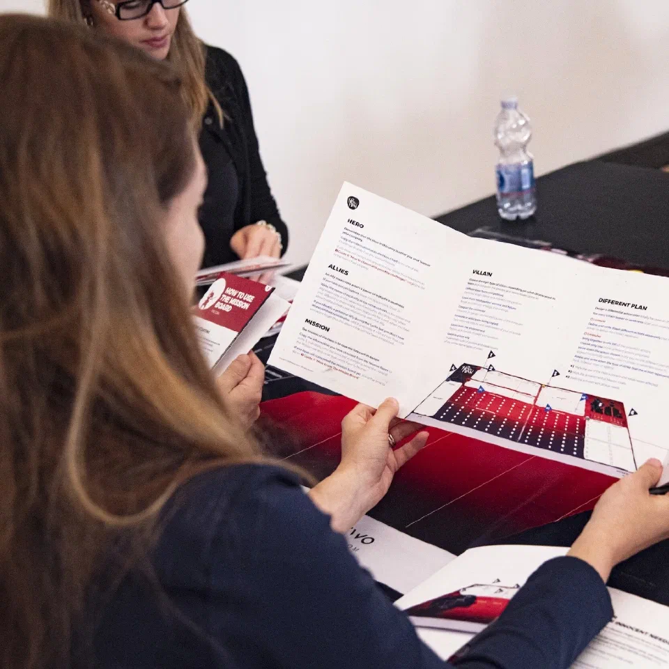 Two people at a table reading a printed brochure and a folded mission-board spread
