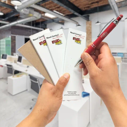 Branded SC Press notepads and a printed pen held in two hands